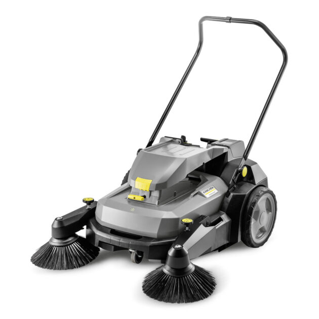 A gray Sweeper KM 70/30 C BP Pack ADV with two large rotary brushes at the front, a sturdy handle, and large rear wheels. The machine has a modern design with various operational controls and small yellow accents.