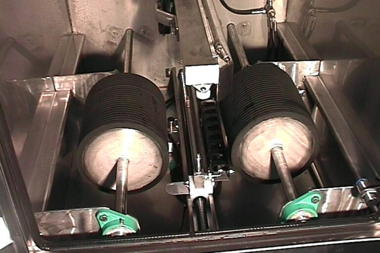 Interior of a machine showing two large cylindrical rollers, possibly part of an industrial or manufacturing process, set within a metallic housing.
