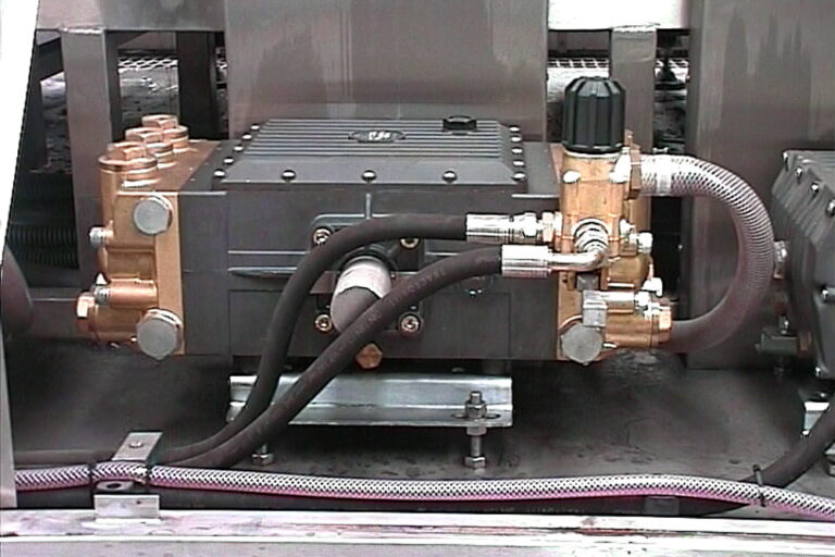 An industrial setup featuring a metallic device with various connected hoses and copper fittings, placed on a sturdy platform with adjoining machinery parts visible.