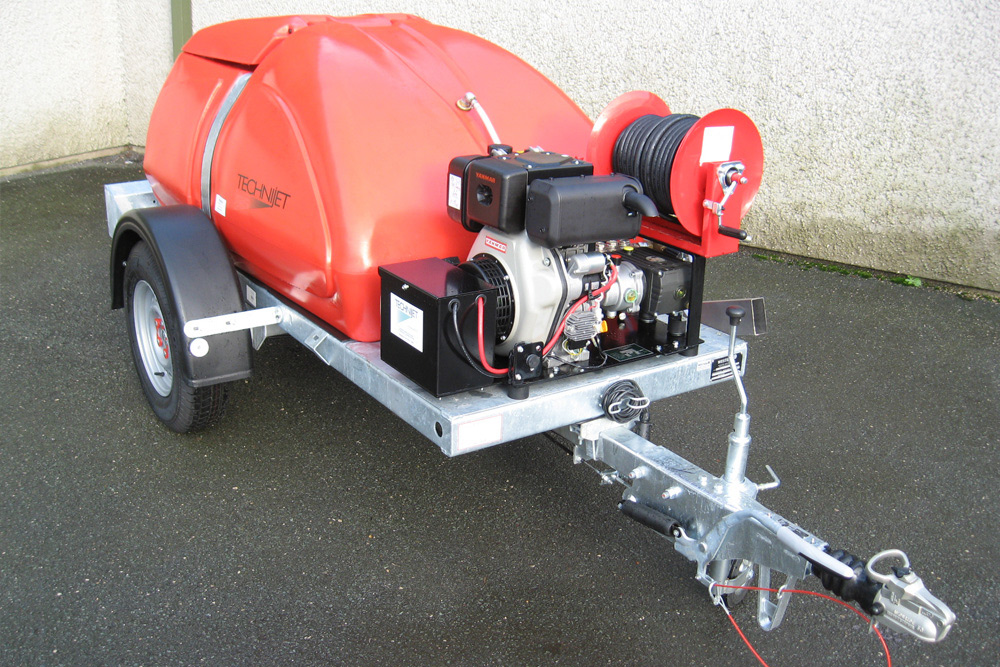 A red industrial pressure washer system mounted on a small gray trailer equipped with a motor, hose reel, and other operational controls.