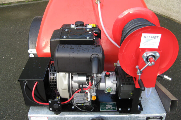 Red and black high-pressure water jetting machine with a prominent motor, reels, and attached hoses, mounted on a metal base.
