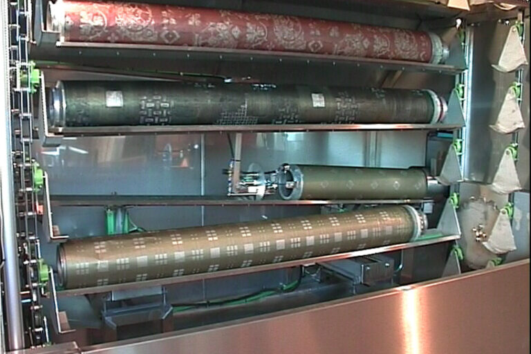 Interior of a printing press showing several cylindrical rollers with patterns, used for applying ink to materials in the printing process.