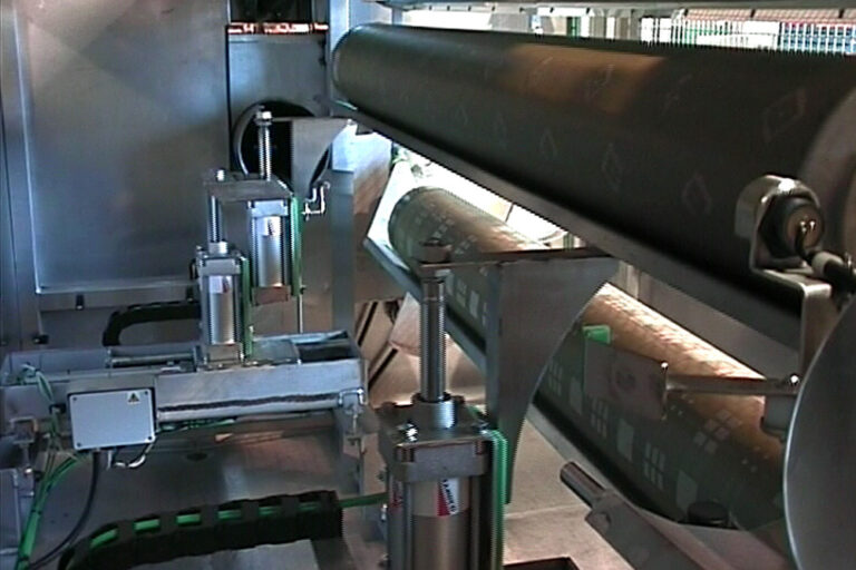 Industrial machine with large cylindrical rollers processing material, featuring metallic structures and mechanical components in a factory setting.
