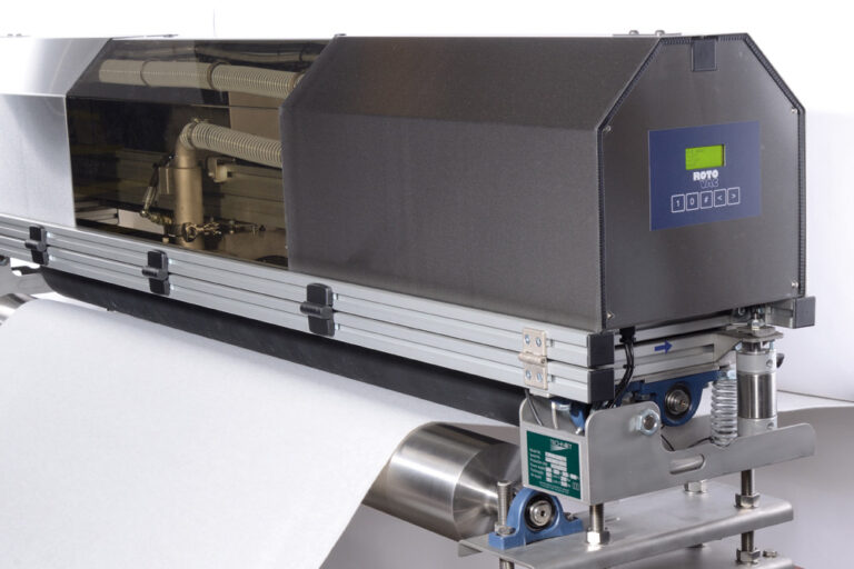 An industrial textile printer with a digital display and a roll of white fabric, set on a metal track system.